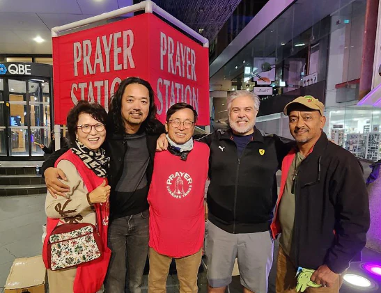 Equipe multicultural reunida diante da faixa do Prayer Station